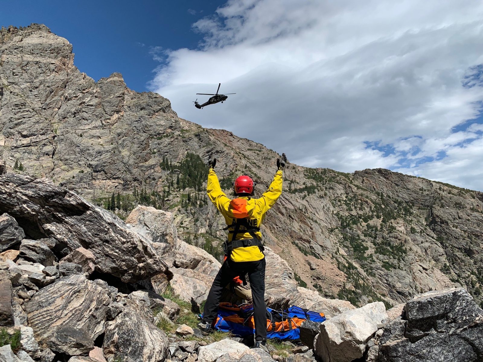 Search and rescue worker signaling on a rocky mountain slope as a helicopter approaches