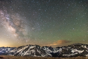 A star-filled night sky with the Milky Way visible above snow-capped mountains and ridges.