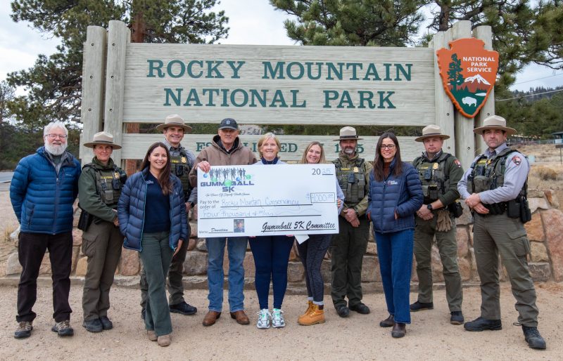 Rocky Mountain Conservancy and National Park Service staff receive a donation at the Rocky Mountain National Park entrance sign.