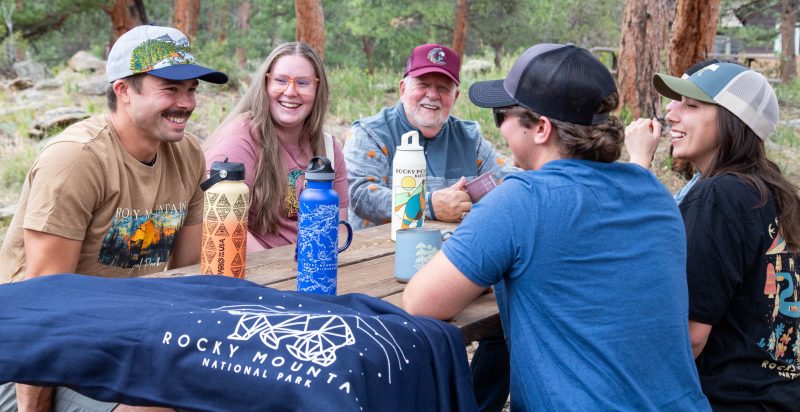 A group wearing Rocky Mountain National Park apparel gathers around a picnic table.